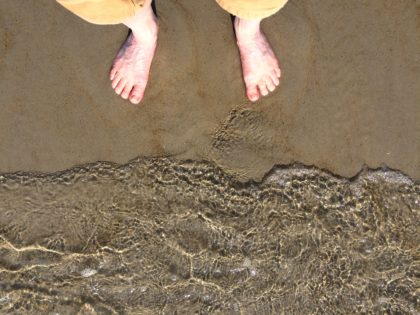 Waves ripple down the shore from two bare feet.